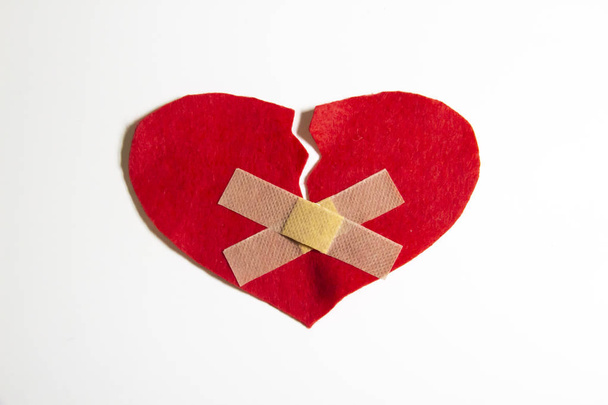 Broken heart and glued together with a band-aid. A heart from felt. A concept about broken love. Heart with plaster isolated on white background - Foto, Bild