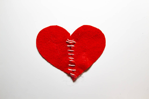 Összevarrtam egy összetört szívet egy cérnával. A vörös szív filcből van. Összetört szerelem koncepció. Rögzített szív cérnával. - Fotó, kép