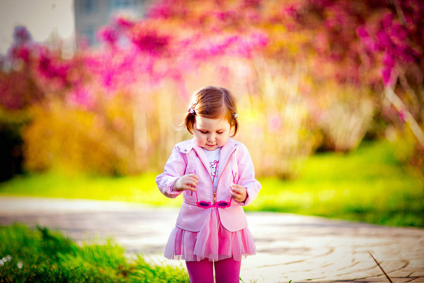a small, beautiful girl in pink clothes and sunglasses, walking in the Park - Foto, afbeelding