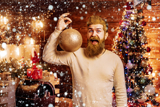 Santa Claus in Santa hat hold Christmas gift. Santa at home with Christmas bag. Bearded man having fun near Christmas tree indoors. Home Christmas atmosphere. - Photo, image