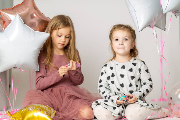 two blonde little sisters play sitting on the floor in a photo studio - Foto, afbeelding