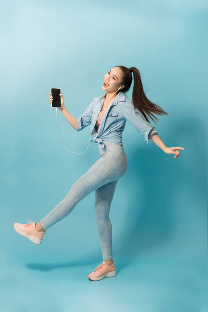 Joyeuse femme asiatique satisfaite dans les écouteurs écoutant de la musique et sautant sur fond bleu
 - Photo, image