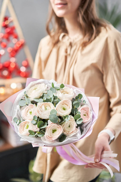 Persian buttercup in womans hands. Bunch pale pink ranunculus flowers with green eucalyptus. The work of the florist at a flower shop - Fotografie, Obrázek