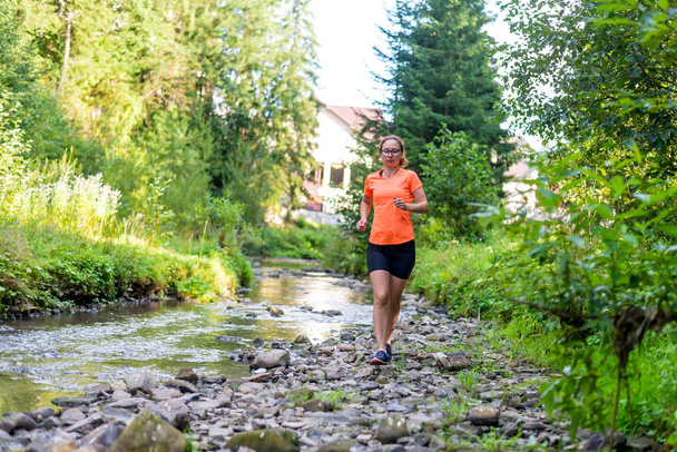 Κορίτσι σε ένα φωτεινό πορτοκαλί T-shirt τρέχει κατά μήκος ενός ποταμού βουνό. - Φωτογραφία, εικόνα