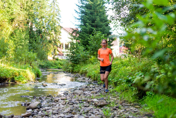Девушка в ярко-оранжевой футболке бежит вдоль горной реки
. - Фото, изображение