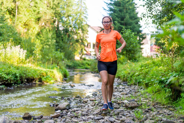 Κορίτσι σε ένα φωτεινό πορτοκαλί T-shirt τρέχει κατά μήκος ενός ποταμού βουνό. - Φωτογραφία, εικόνα