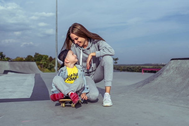 Woman mother encourages and motivates child on skateboard, little boy 3-5 years old, summer sports field in city, autumn, learns to ride skateboard, emotions love, care, relaxation enjoyment. - Фото, зображення