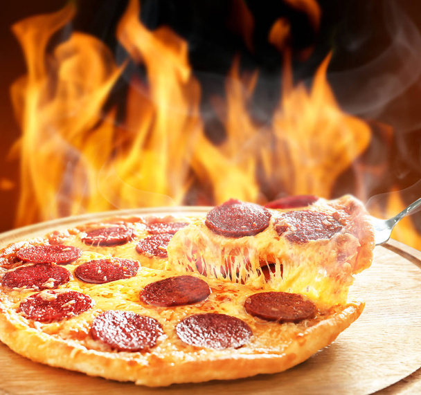 Toma de rebanada de pizza caliente de tablero de madera contra llama ardiente
 - Foto, imagen