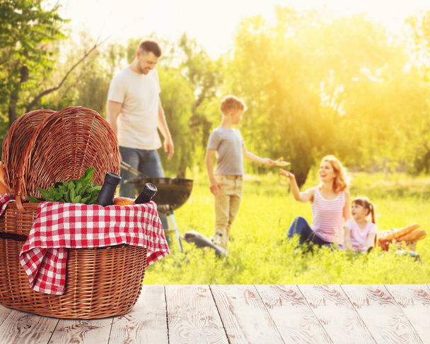 Fonott kosár ízletes ételek és italok az asztalon közel boldog család a nyári piknik - Fotó, kép