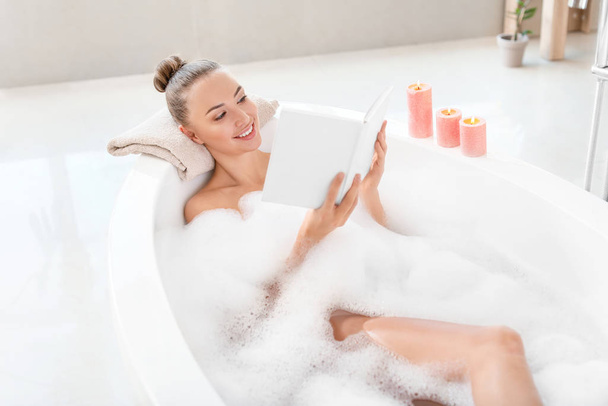Beautiful young woman reading book in bathtub - Photo, Image