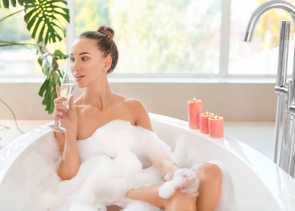 Beautiful young woman drinking champagne in bathtub - Fotó, kép