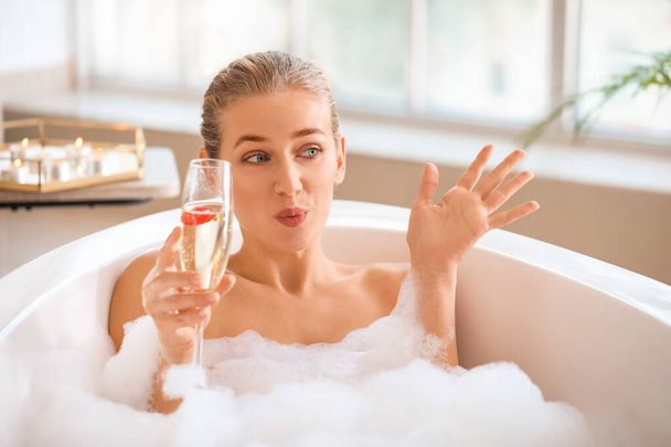 Gyönyörű fiatal nő pezsgőt iszik a fürdőszobában - Fotó, kép