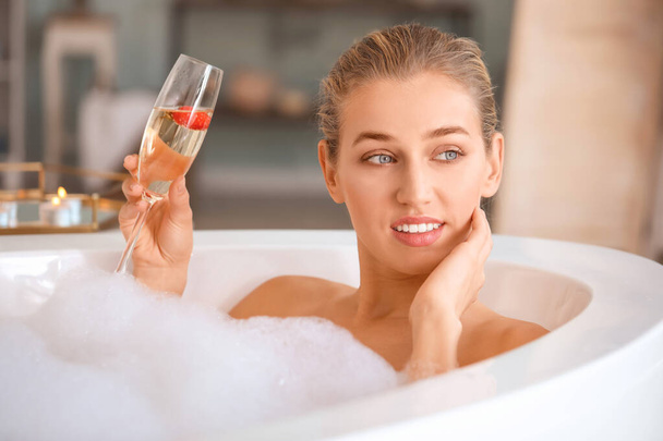 Beautiful young woman drinking champagne in bathroom - 写真・画像