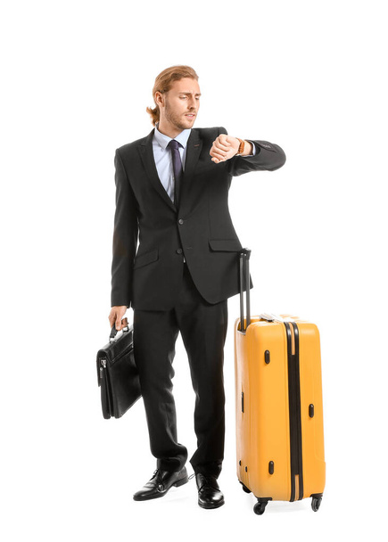 Jeune homme d'affaires avec des bagages regardant la montre, isolé sur blanc
 - Photo, image