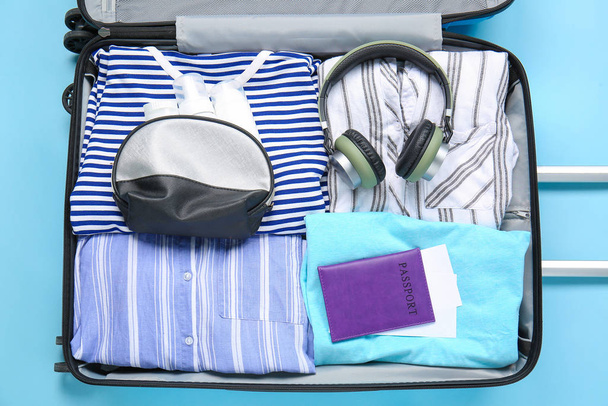 Βαλίτσα με συσκευασμένα ρούχα, διαβατήριο και αξεσουάρ στο φόντο χρώμα - Φωτογραφία, εικόνα