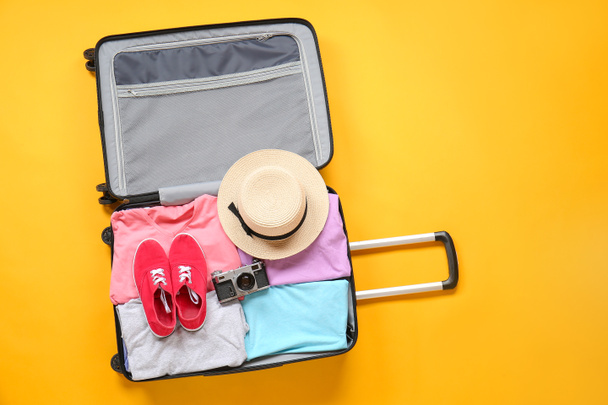 Βαλίτσα με συσκευασμένα ρούχα και φωτογραφική μηχανή φωτογραφία στο φόντο χρώμα - Φωτογραφία, εικόνα