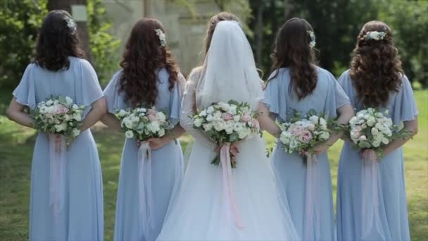 Rear view of bride and four bridesmaids standing and holding bouquets behind their backs - 映像、動画