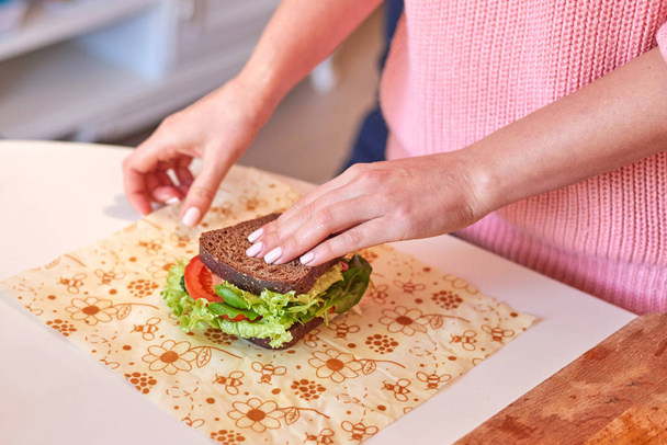 Женские руки заворачивают здоровый сэндвич в пищевую плёнку из воска
 - Фото, изображение