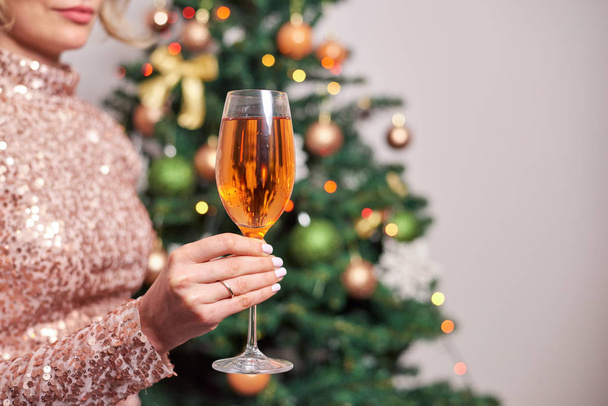 Woman holding glass of champagne with christmas tree on background - Foto, Imagem