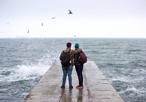 zwei Freunde sitzen an der Seebrücke und beobachten das Meer - Foto, Bild