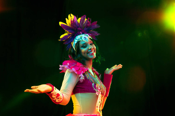 Beautiful young woman in carnival mask and masquerade costume in colorful lights - Photo, Image