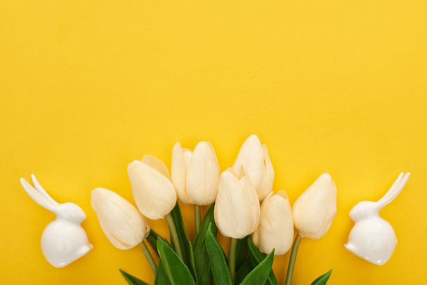πάνω όψη τουλίπες και λευκά λαγουδάκια Πάσχα σε πολύχρωμο κίτρινο φόντο - Φωτογραφία, εικόνα
