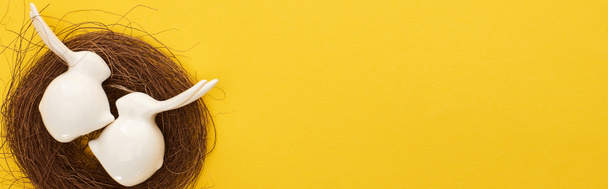 vista superior de conejitos de Pascua blancos figuritas en nido sobre fondo amarillo colorido con espacio para copiar, plano panorámico
 - Foto, Imagen