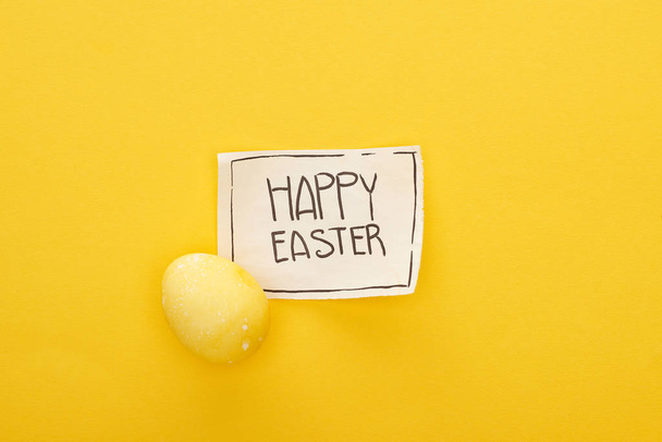 top view of greeting card with happy Easter lettering and painted egg on yellow colorful background - Photo, Image