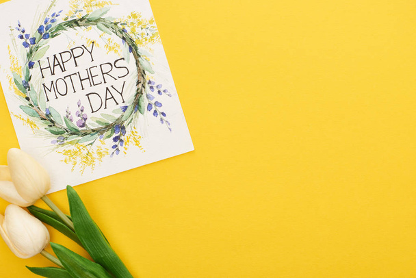 widok z góry wiosna tulipany i szczęśliwy dzień matki kartka okolicznościowa na kolorowe żółte tło - Zdjęcie, obraz