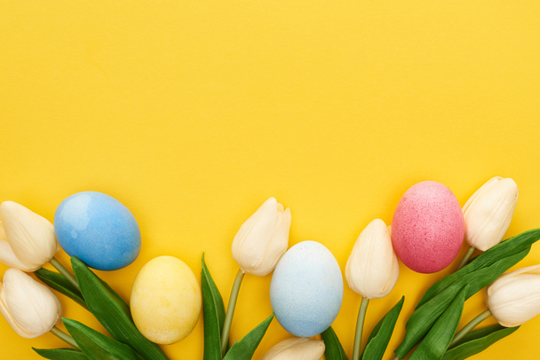 top view of tulips and painted Easter eggs on colorful yellow background - Foto, Bild