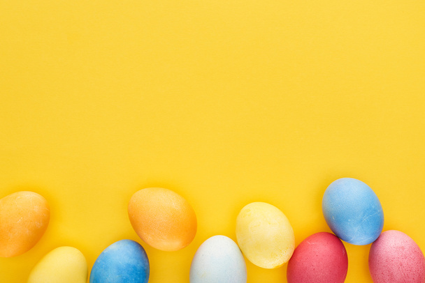 top view of multicolored painted Easter eggs on yellow background with copy space - Foto, Imagen