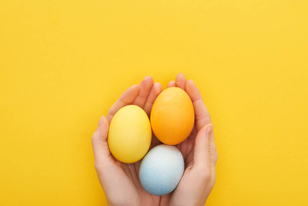cropped view of woman holding multicolored painted Easter eggs on yellow background - Фото, зображення