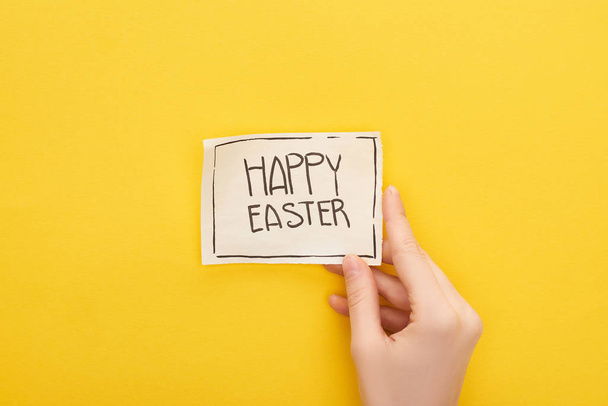 cropped view of woman holding greeting card with happy Easter lettering on yellow background - Foto, Imagem