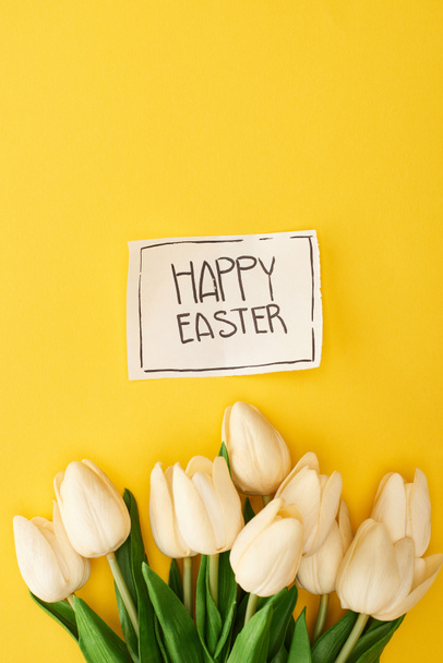 vista superior de los tulipanes y la tarjeta de felicitación con letras de Pascua feliz sobre fondo amarillo colorido
 - Foto, imagen