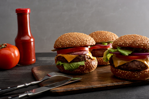 delicious fresh meat cheeseburgers on wooden board near cutlery and ketchup - Photo, Image