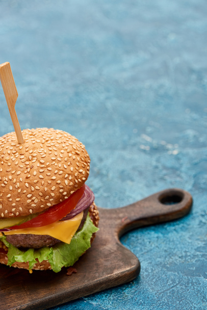 delicious cheeseburger on wooden board on blue textured surface - Фото, изображение