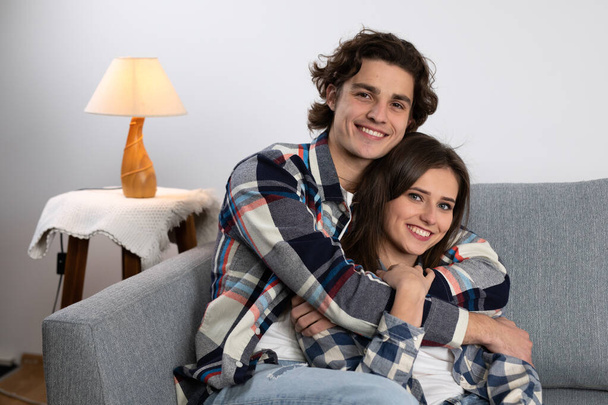 Smiling young man embracing girlfriend on couch - Foto, afbeelding