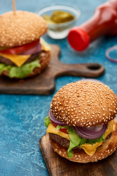 selective focus of delicious cheeseburger on wooden board on blue textured surface - Photo, Image