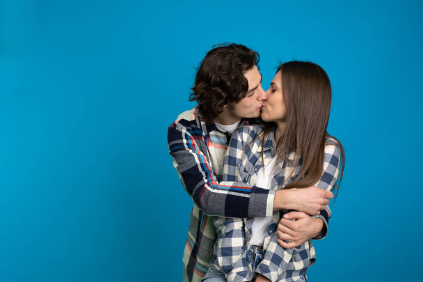 Couple in checkered shirts embracing and kissing isolated on blue background - 写真・画像