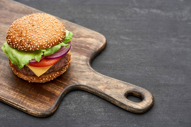 delicious fresh cheeseburger on wooden board on grey surface - Photo, Image
