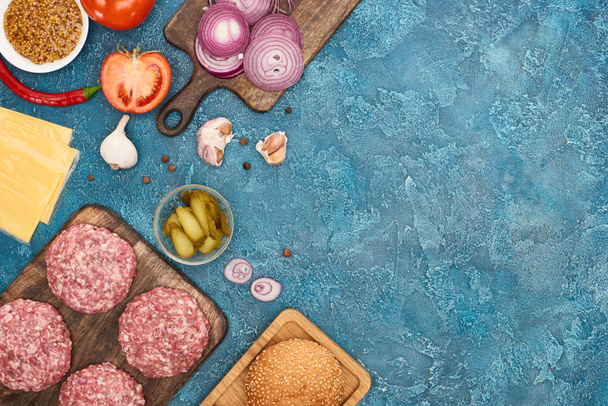 vista superior de los ingredientes frescos de la hamburguesa en la superficie texturizada azul con espacio de copia
 - Foto, imagen