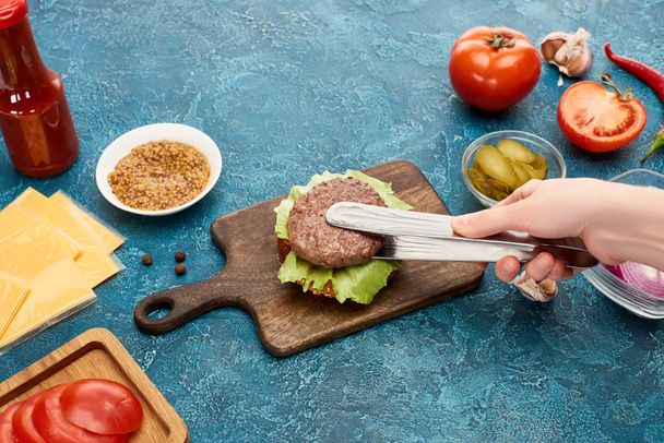 cropped view of woman cooking delicious fresh burger on blue textured surface - Photo, Image