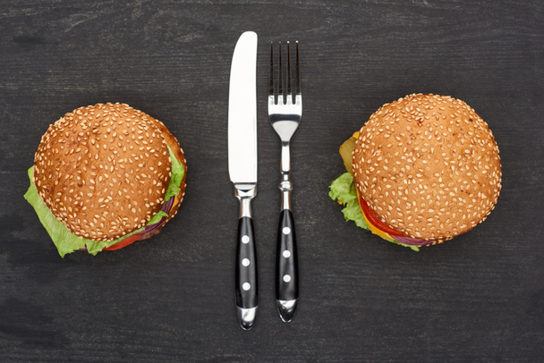 tasty fresh burgers on wooden black table with cutlery - Photo, Image