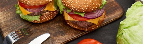 tasty fresh cheeseburgers on wooden board with cutlery, panoramic shot - Photo, Image