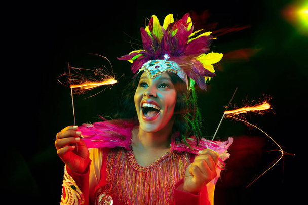 Beautiful young woman in carnival mask and masquerade costume in colorful lights - Fotografie, Obrázek
