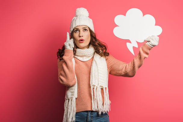 thoughtful girl in warm hat and scarf showing idea sign while holding thought bubble on pink background - Photo, Image