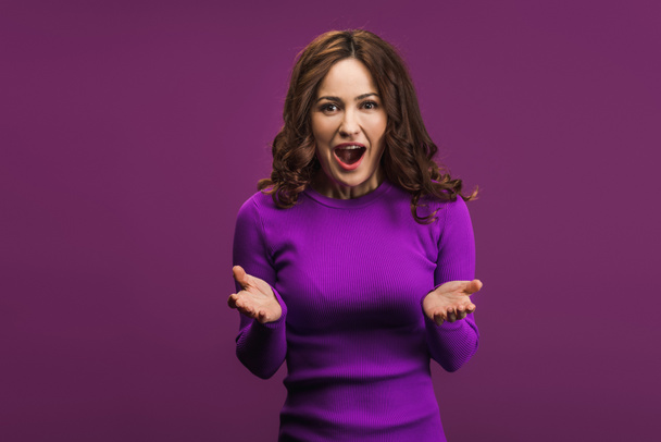 excited woman standing with open arms and looking at camera on purple background - Valokuva, kuva