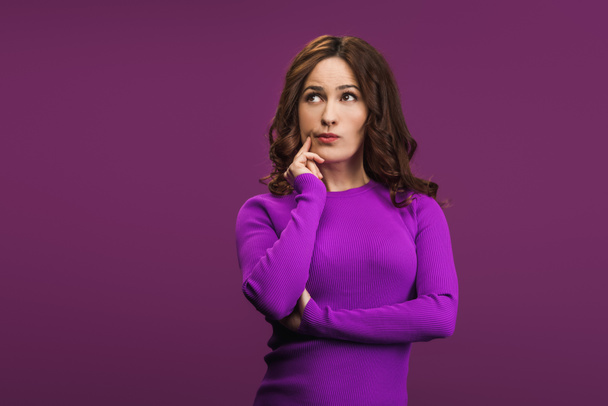 mujer pensativa tocando la cara y mirando hacia otro lado sobre fondo púrpura
 - Foto, Imagen