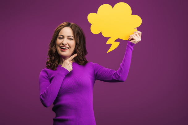 cheerful woman pointing with finger at thought bubble on purple background - Photo, Image