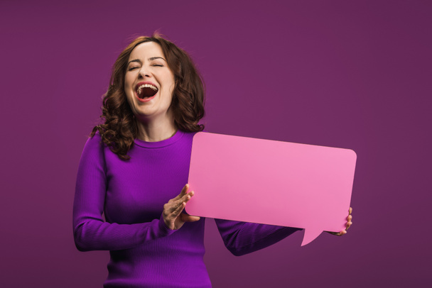 cheerful woman laughing while holding speech bubble on purple background - Photo, Image